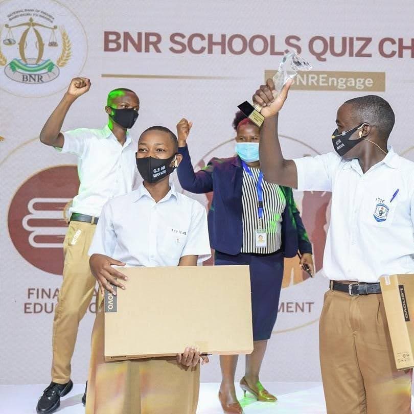 Students celebrating on stage at the National Bank of Rwanda Schools Quiz Challenge final, one holding a trophy aloft, others holding prizes.