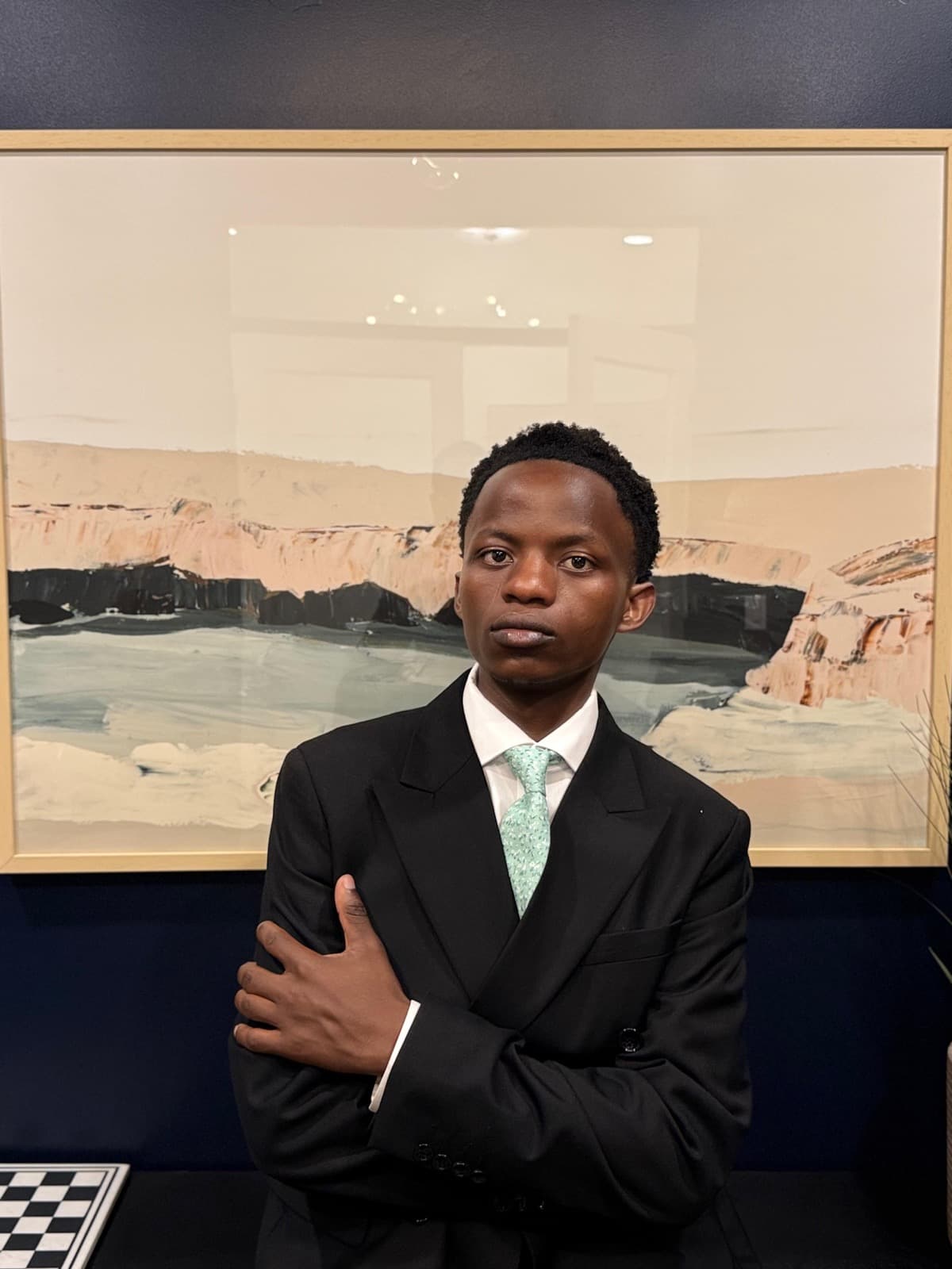 Evode Manirahari, arms folded, in front of a framed landscape painting.