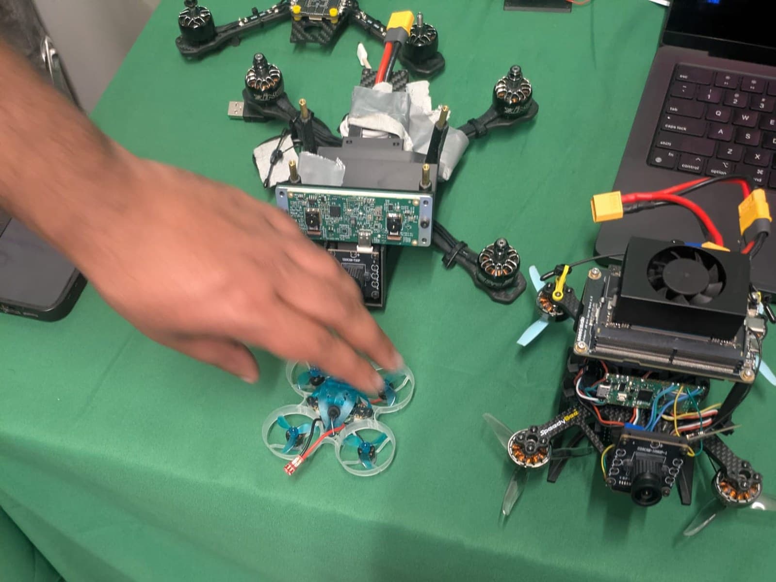 Three quadcopters on a workbench: a carbon-fibre FPV frame, a small ducted trainer, and a larger airframe carrying a fan-cooled NVIDIA Jetson Orin and a forward-facing camera.